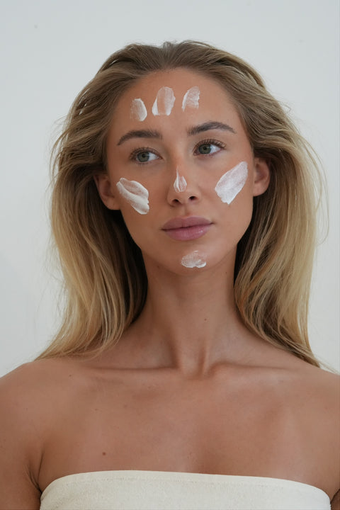 Une femme aux cheveux pâles s'applique de la crème dans le visage.