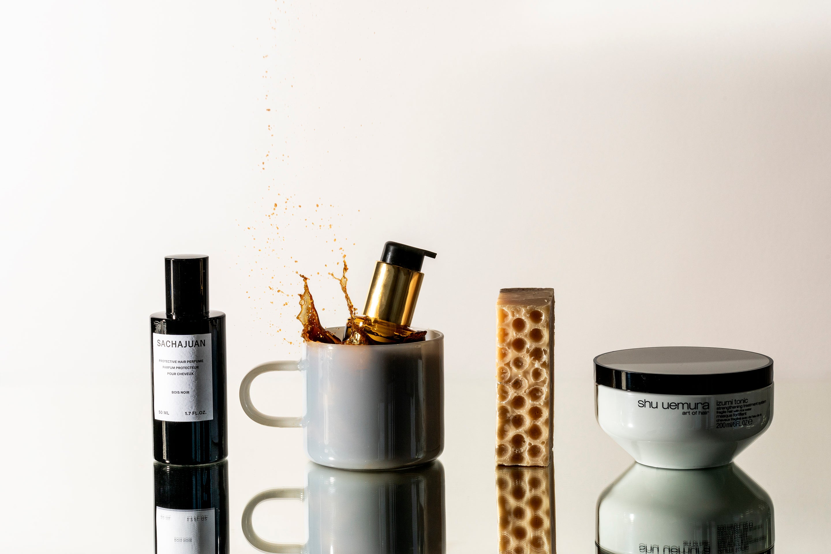 De gauche à droite, on retrouve le parfum capillaire Bois Noir de Sachajuan, l'huile Elixir Ultime de Kérastase qui plonge dans un café noir, une barre de savon et le masque fortifiant Izumi de shu uemura.